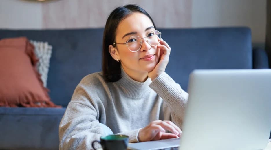 Woman wearing Specscart round blue light glasses while using a laptop at home, illustrating comfortable protection from digital eye strain.