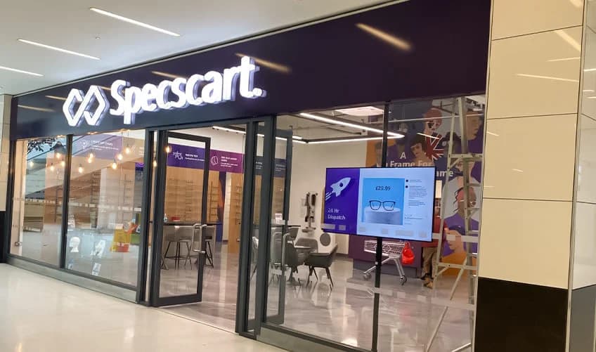 Specscart Walkden storefront with a prominent glowing purple sign and a digital window display advertising 24-hour dispatch on quality eyewear.