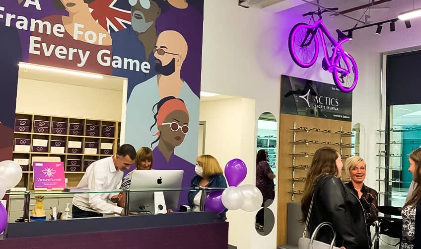Vibrant Specscart Walkden interior featuring a purple bicycle wall mount, colourful mural, and friendly staff at the service counter with balloons.