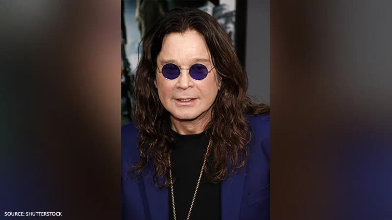 Ozzy Osbourne wearing his signature small, round purple-tinted sunglasses, a blue blazer, and a gold chain, showcasing his iconic rock star aesthetic.