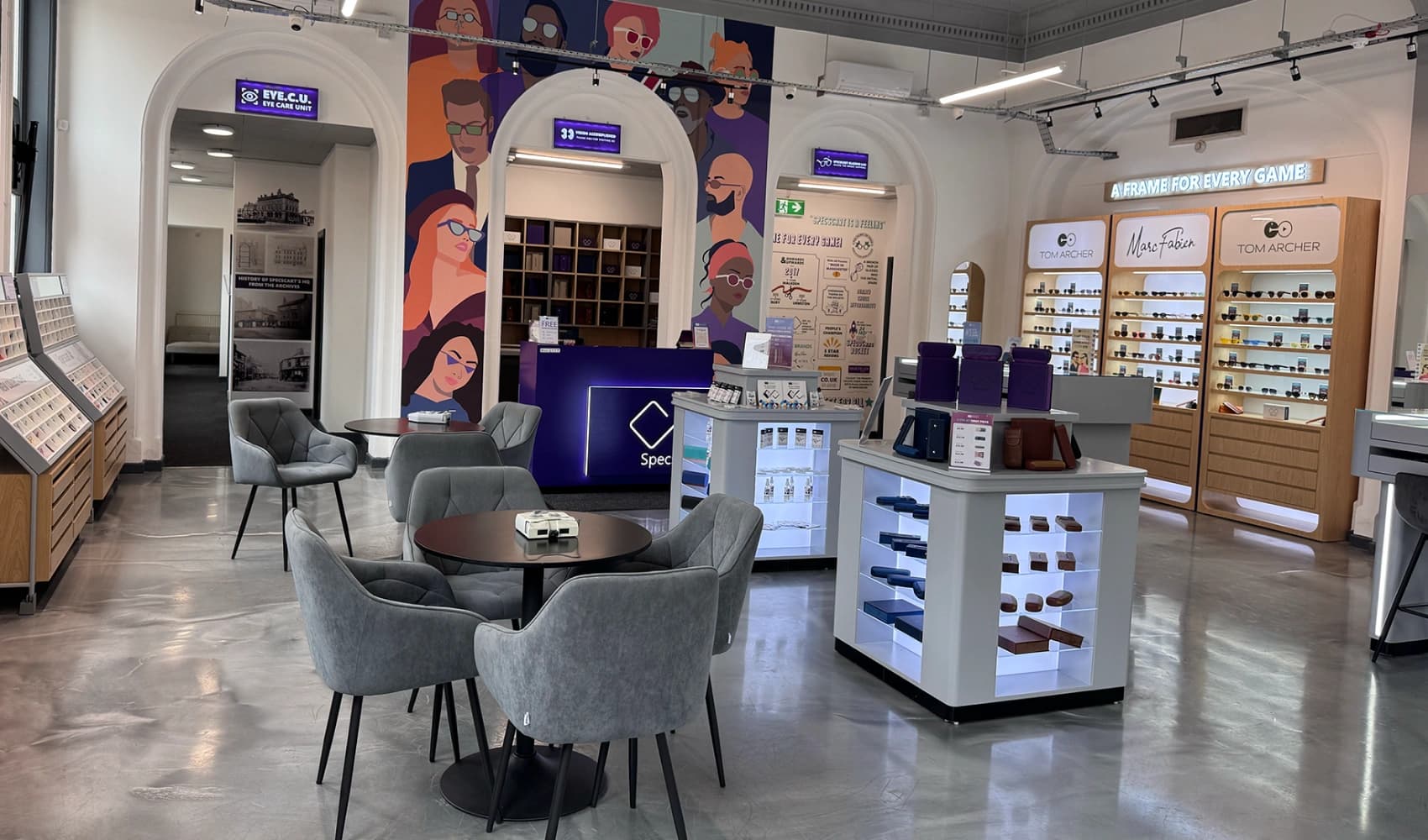 Specscart Bury interior featuring stylish grey seating, a vibrant wall mural, and glowing displays of Tom Archer and Marc Fabien designer eyewear.