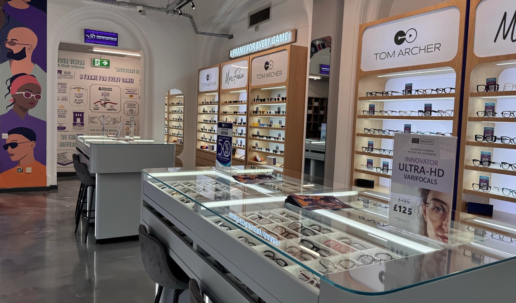 Detailed view of Specscart Bury interior with glass display counters, wooden eyewear racks, and signs for premium Ultra-HD varifocal lens options.