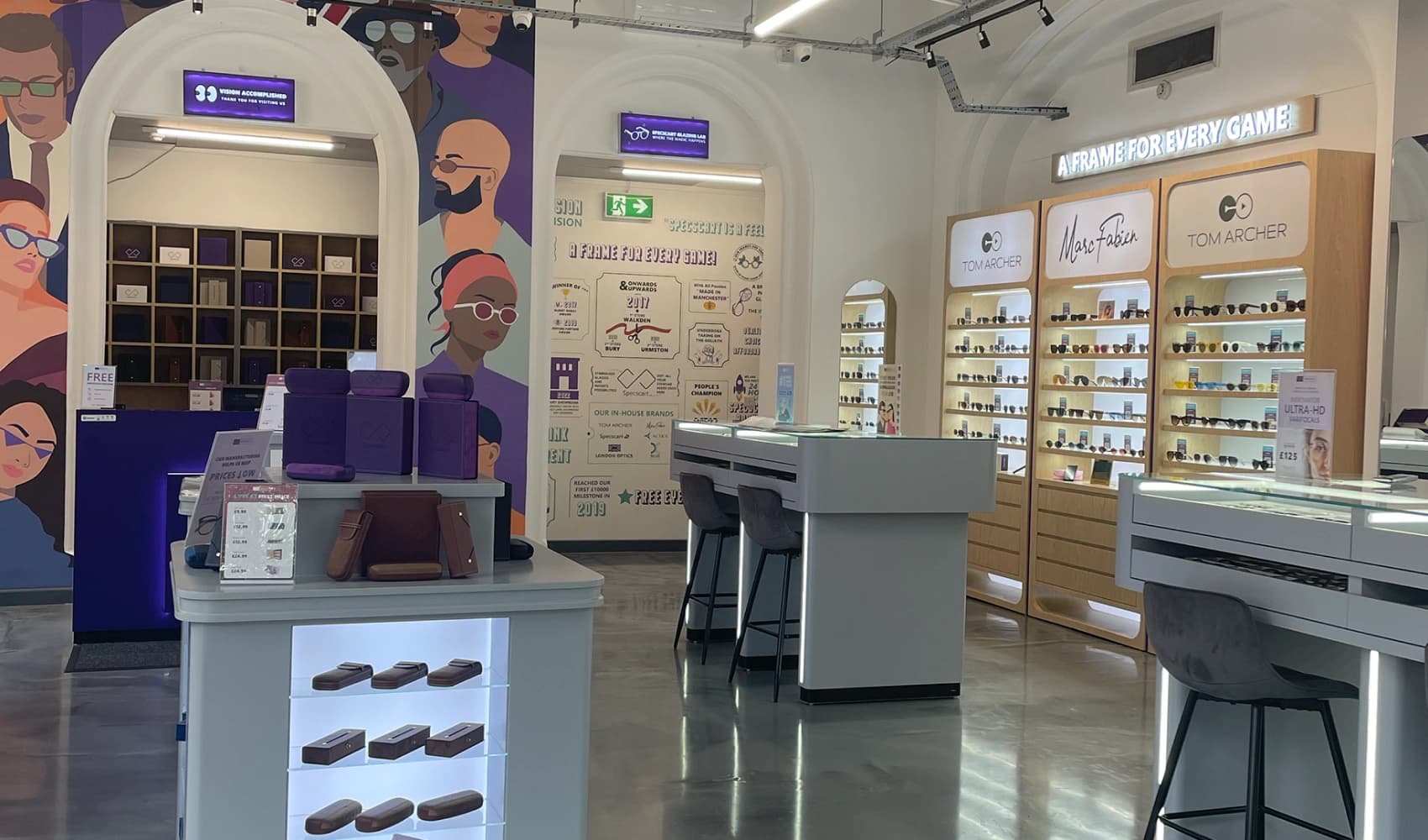 Modern interior of Specscart Bury store showcasing minimalist furniture, white arched walls, and premium designer frames displayed on lit shelving.