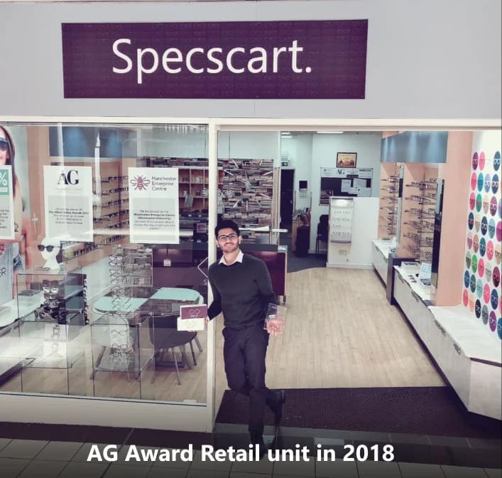 Front entrance of Specscart retail unit in 2018, with a prominent purple Specscart sign, eyewear displays, and glass doors. Specscart founder Sid Sethi stands at the entrance holding a certificate, highlighting the AG Award recognition.