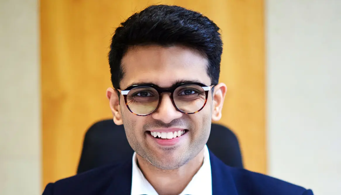 Sid Sethi (Specscart’s founder) in business attire seated in front of a warm wooden backdrop. The image highlights his achievement of being named in the Forbes 30 Under 30 Europe for Retail and Ecommerce in 2024 list.