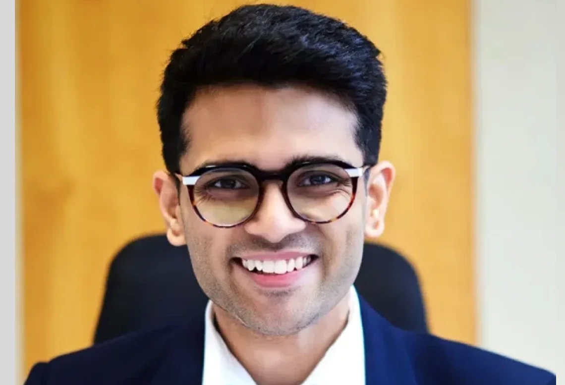 Business portrait of Sid Sethi, Specscart’s founder, seated in front of a wooden background. The image accompanies text celebrating his inclusion in the Forbes 30 Under 30 Europe list for 2024.