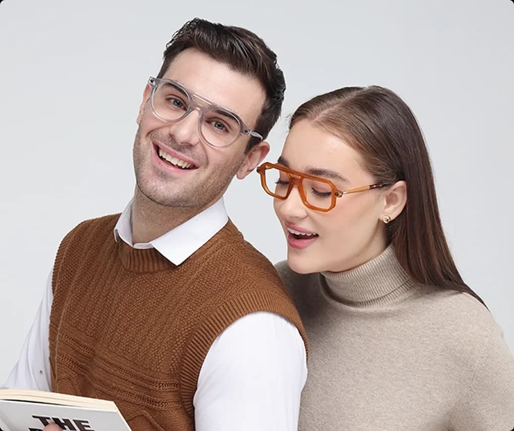 A man and woman wearing Specscart glasses with Transitions lenses in their clear indoor state, featuring stylish transparent and amber navigator frames.