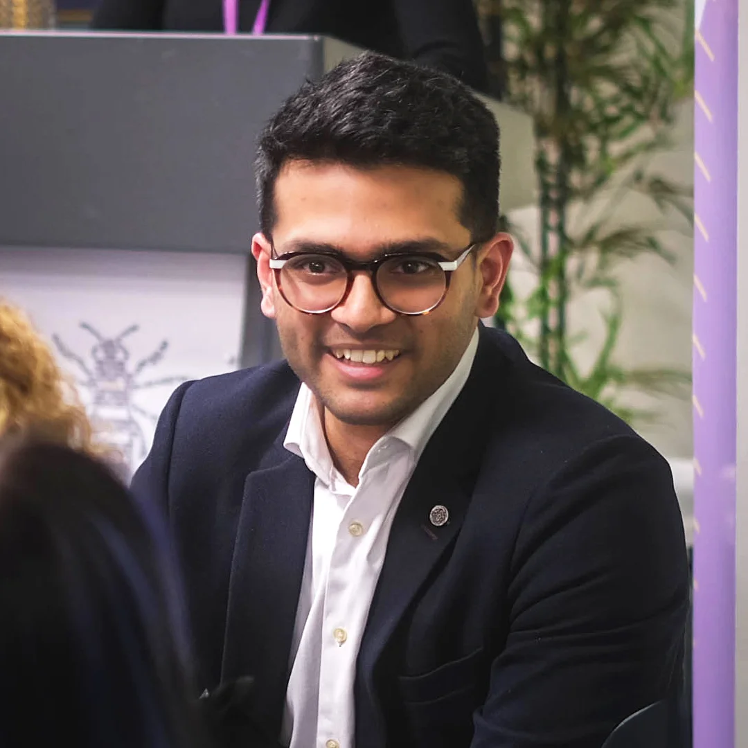 Sid Sethi, founder of Specscart, in a business event setting, dressed in a dark blazer and white shirt, seated at a table with a presentation board and attendees in the background.