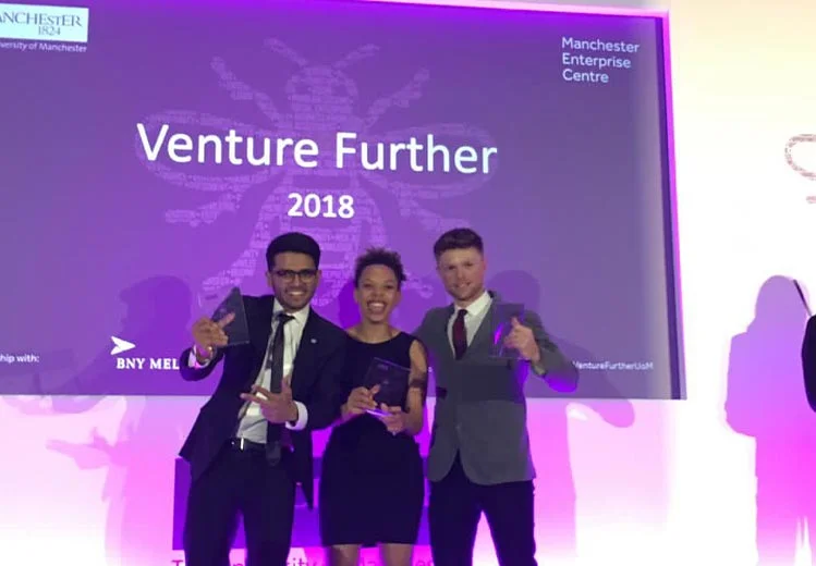 Awards ceremony group photo at Venture Further 2018, with Sid Sethi, Specscart’s founder, and two other people in formal attire posing in front of a large event screen displaying the Manchester Enterprise Centre branding.