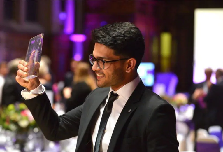 Sid Sethi, Specscart’s founder, dressed in a suit and tie, holding up the Venture Further Award trophy at a formal event in 2018. The background shows an elegant venue with guests, capturing a milestone moment for the company.