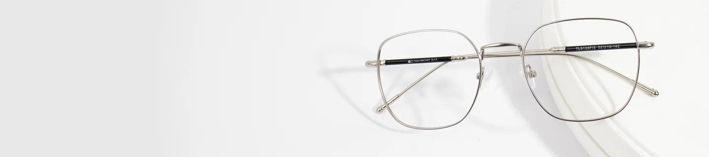 Titanium Glasses Lightweight silver titanium glasses with thin geometric frames resting on a clean white background, showcasing a durable and minimalist design.