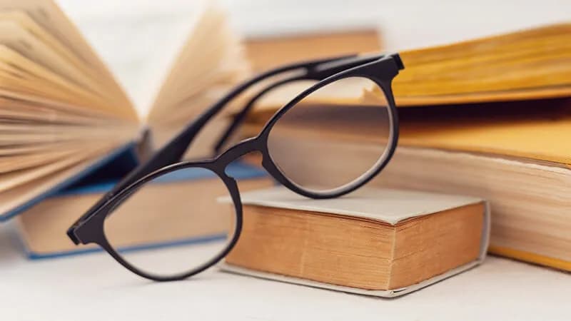 Prescription vs Non-Prescription Reading Glasses Stylish black round-framed glasses resting on a stack of books, representing the essential role of reading glasses for book lovers and students.