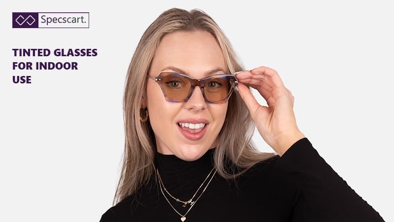 Tinted glasses for indoor use: What should you know? A smiling woman with blonde hair wearing geometric cat-eye glasses with brown-tinted lenses and a tortoise-shell frame.