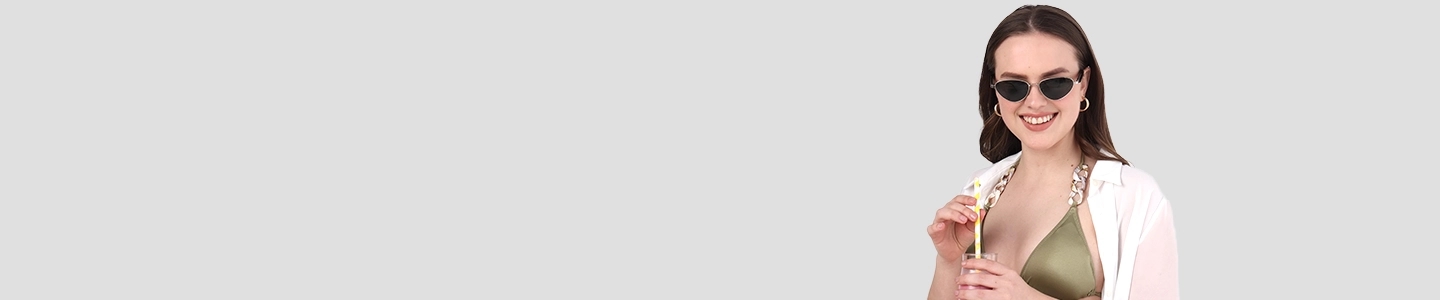 Cat Eye Sunglasses A smiling woman wearing sharp black cat-eye sunglasses, an olive bikini, and a white beach cover-up, holding a summer drink with a yellow straw.