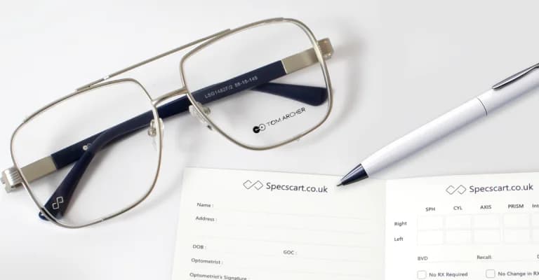 A pair of stylish gold-framed eyeglasses with black temples, resting beside two Specscart prescription pads showing fields for patient details and optical measurements, illustrating the topic of how to read an eyeglasses prescription.