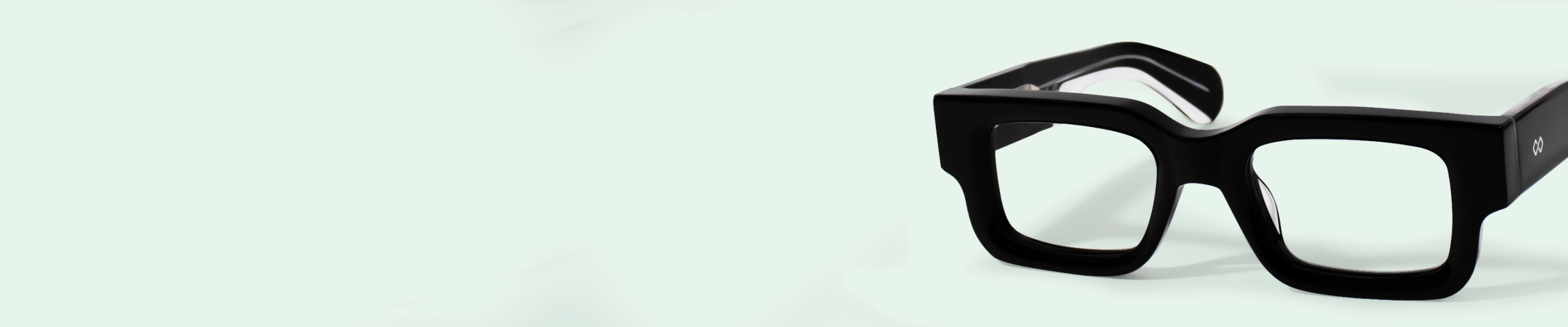 Thick Frame Glasses Close-up of stylish, bold, thick-framed square glasses in glossy black on a pale background.