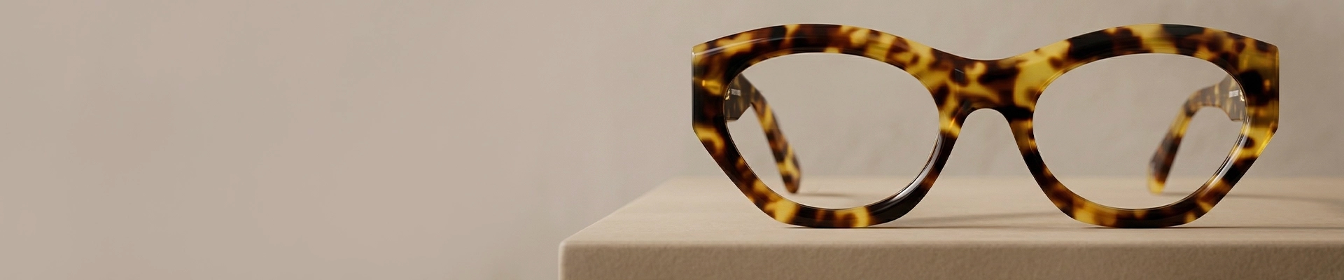 Tortoiseshell Glasses A close-up of stylish, angular tortoiseshell glasses with thick, bold frames, set against a light blue and white background.
