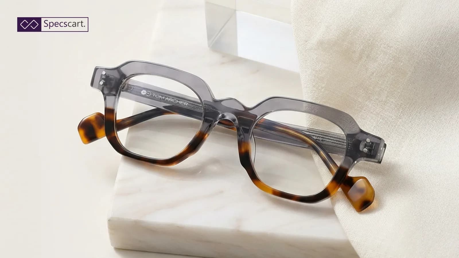 What Are Plano Lenses? Stylish Tom Archer glasses with a grey and tortoiseshell frame resting on a marble slab, showcasing clear plano lenses for a fashion-forward look.